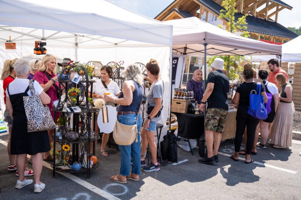 People browse handmade goods under white vendor tents at an outdoor festival.