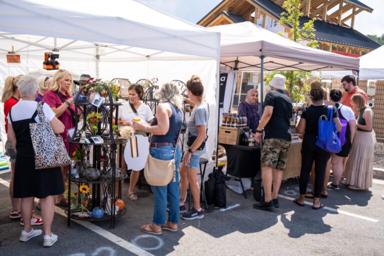 People browse handmade goods under white vendor tents at an outdoor festival.