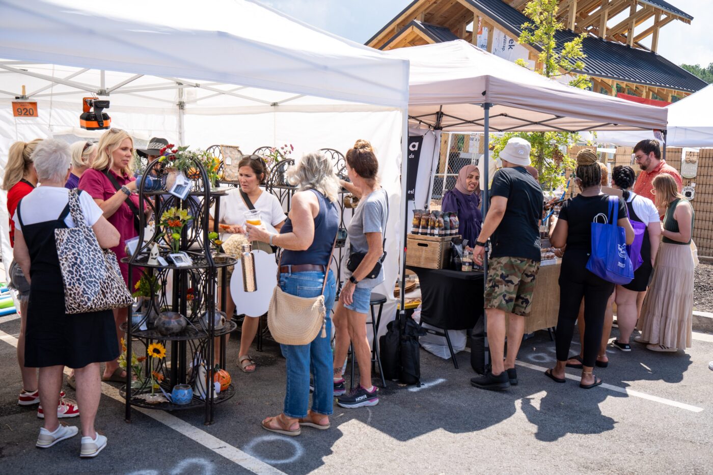 People browse handmade goods under white vendor tents at an outdoor festival.