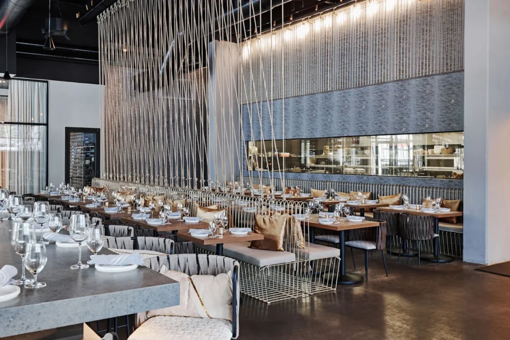 Empty dining room with long wooden tables, wire-framed chairs and hanging rope decor