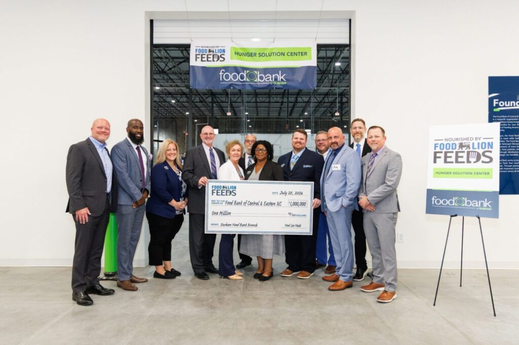 A group of people posing inside a warehouse holding a large ceremonial check in front of Food Lion Feeds and Food Bank banners.