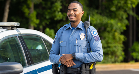 A Gwinnett County police officer stands beside a patrol car outdoors.