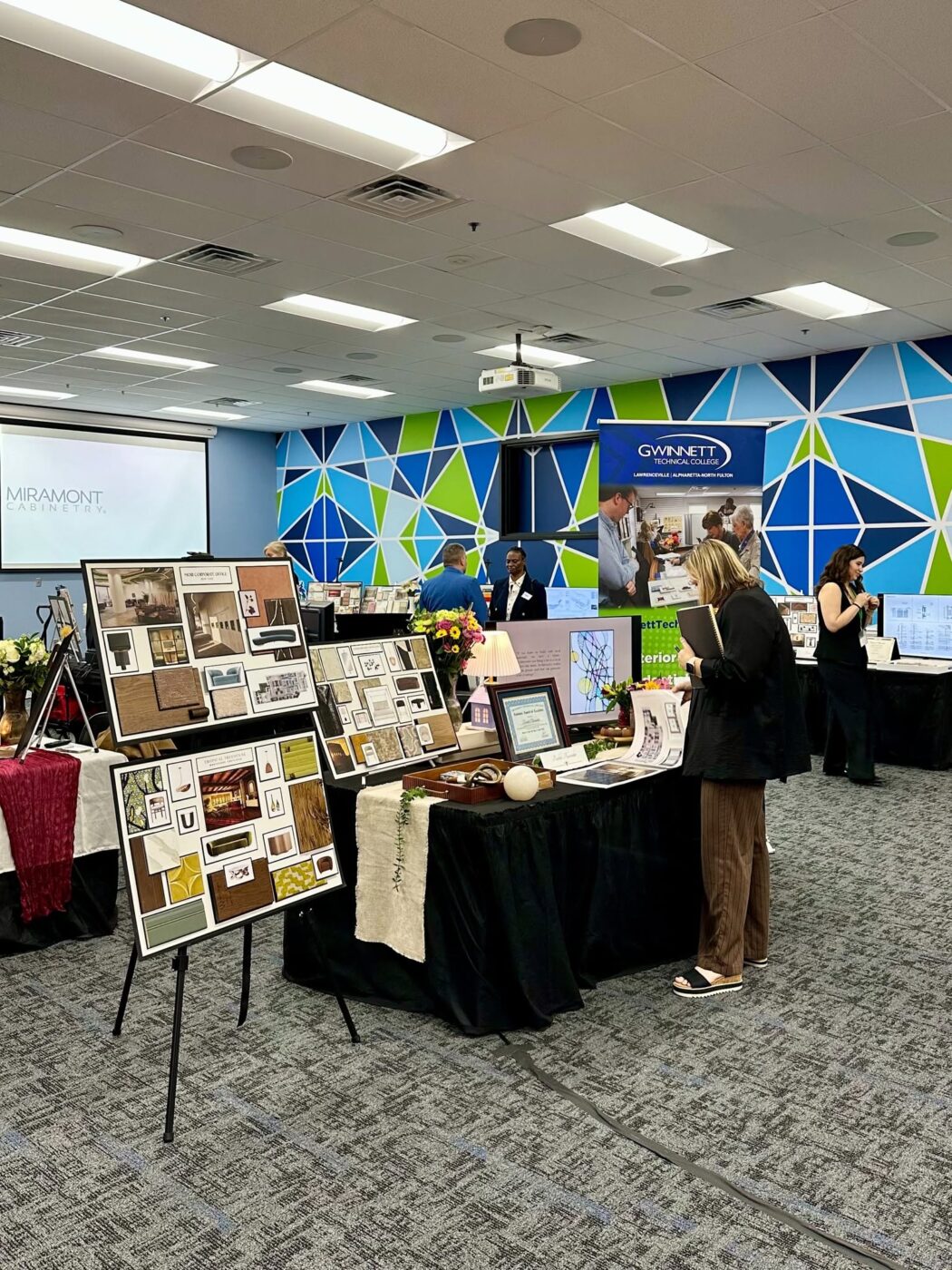 People browse tables and display boards at a college preview event in a classroom or conference room.