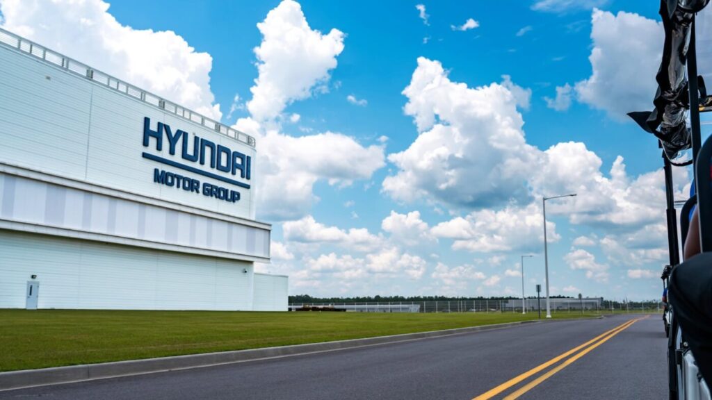Hyundai Motor Group Metaplant America building beside a roadway under a bright sky with large clouds.
