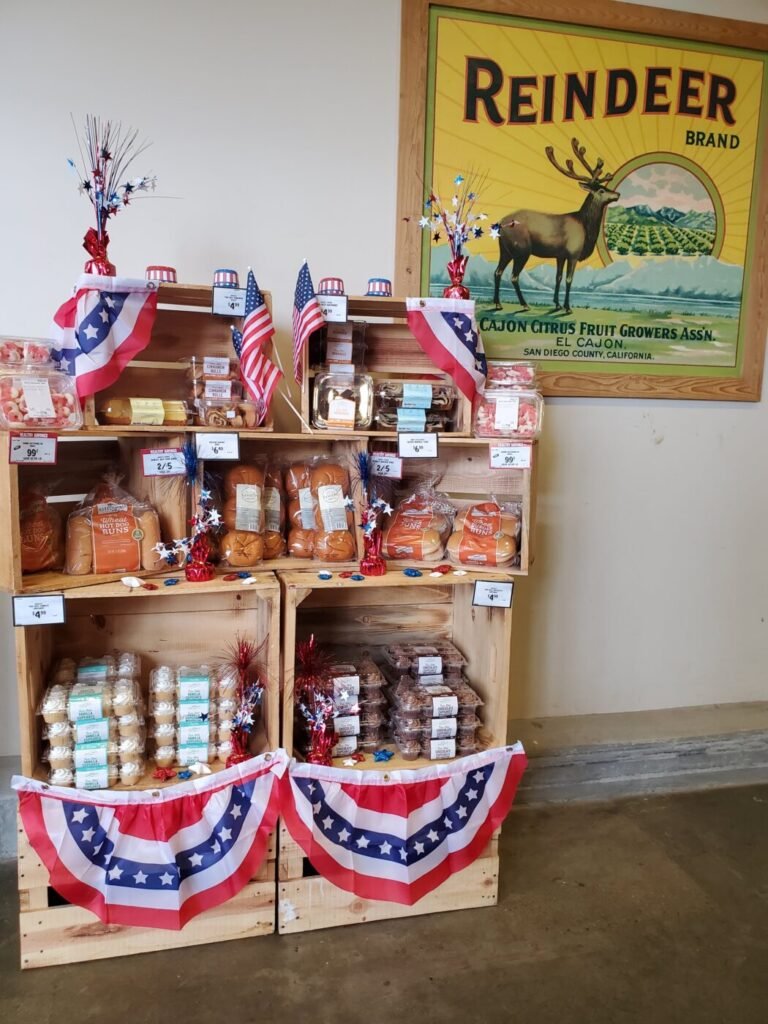 Wooden display of baked goods and snacks decorated with red, white and blue bunting and small American flags beside a wall sign reading Reindeer Brand.