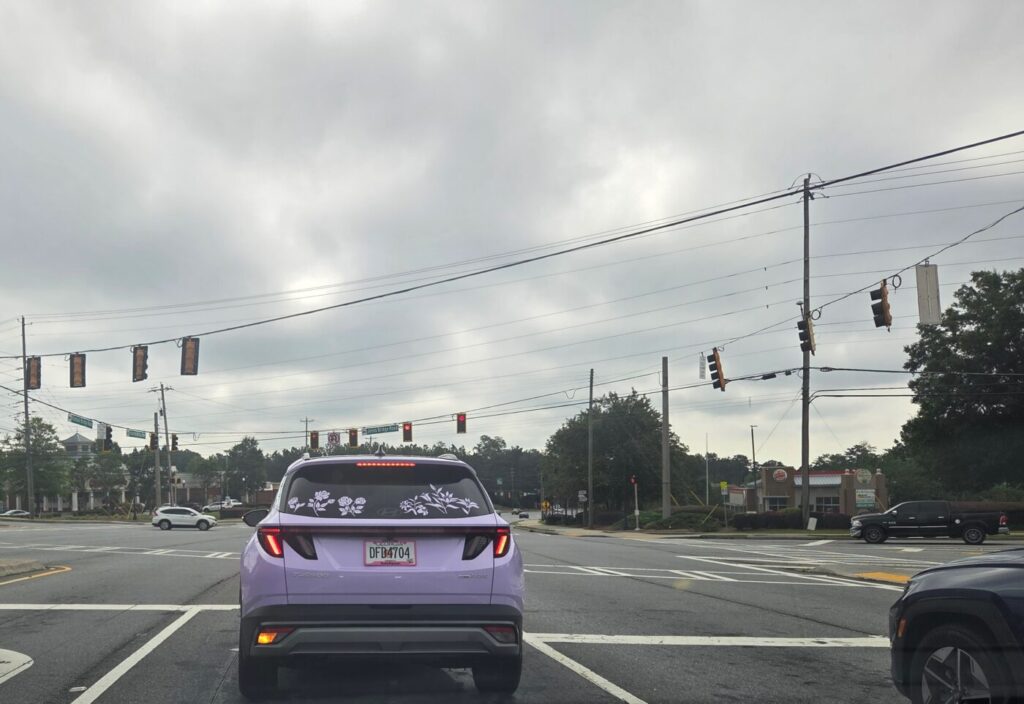 A purple SUV stopped at a red light at a busy intersection