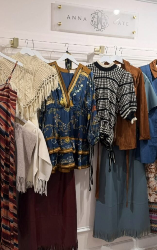 The Johns Creek boutique will carry clothing, shoes, accessories and home décor, including pieces from Anna Cate. Colorful dresses and sweaters hang on a clothing rack beneath an Anna Cate sign.