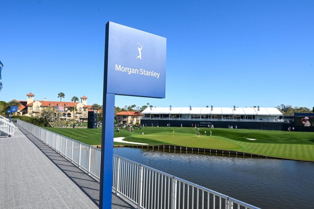 Morgan Stanley sign near a golf course and water hazard under a clear blue sky.