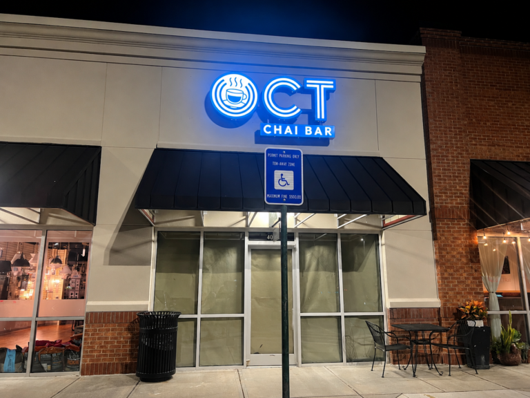 Illuminated OCT Chai Bar sign above a storefront with covered windows and outdoor seating at night.