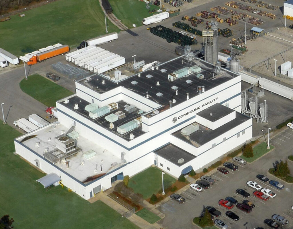 A white industrial building marked compound facility with trucks, trailers and parked cars around it