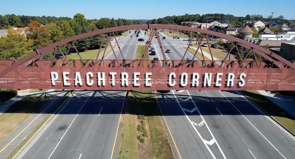 Pedestrian bridge arching over a divided roadway with large letters reading Peachtree Corners