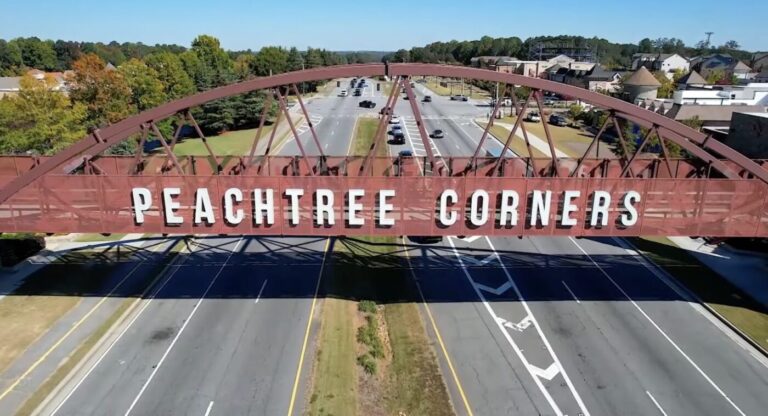 Pedestrian bridge arching over a divided roadway with large letters reading Peachtree Corners