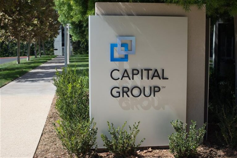 Capital Group sign beside a sidewalk and landscaped greenery outside a building