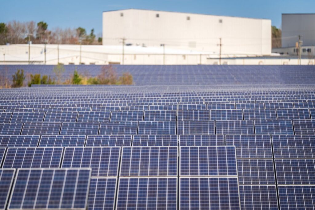 Rows of solar panels in front of a large industrial building
