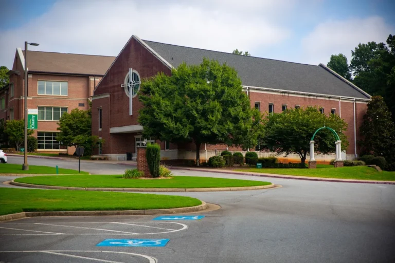 Brick school building with a gabled roof, trees, a landscaped entrance and a curving driveway.