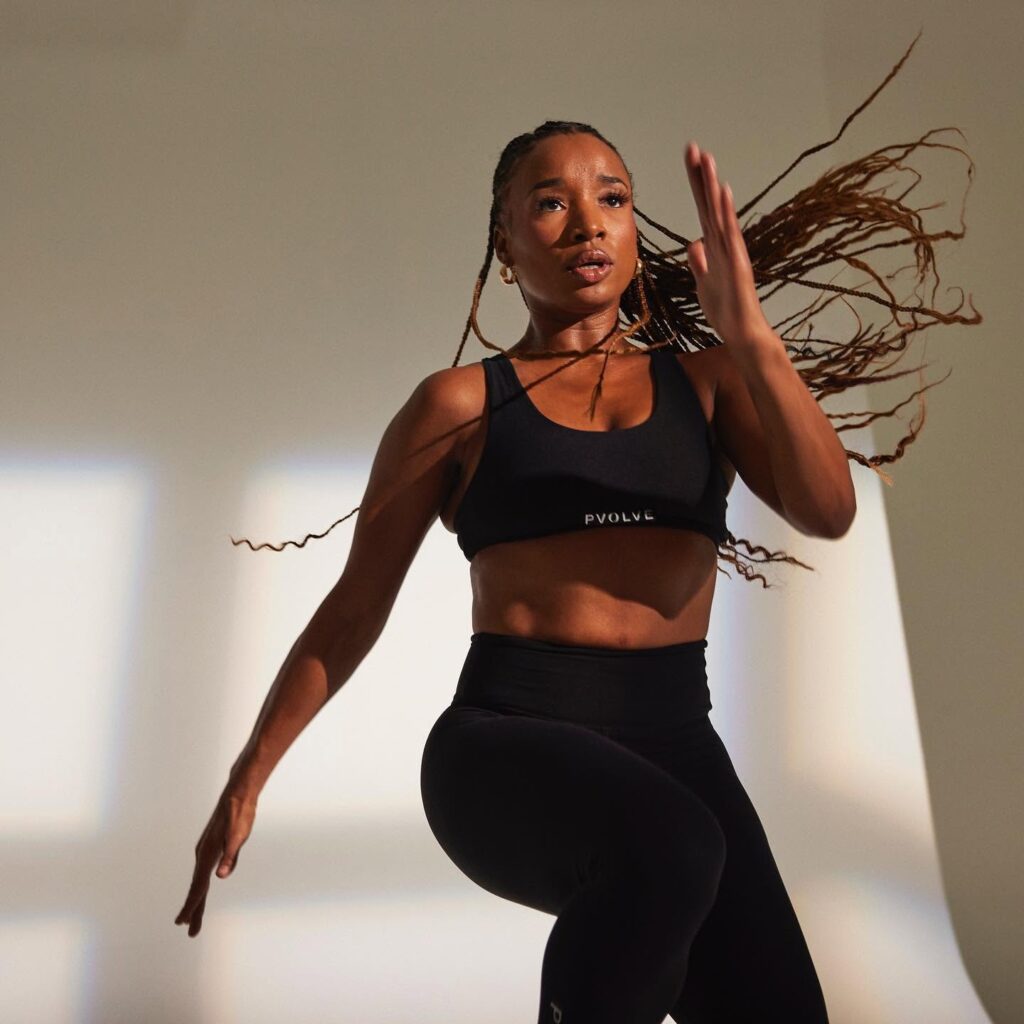 Woman in black workout gear performing a dynamic exercise against a bright studio wall.