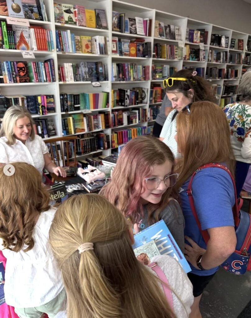 Several shoppers browse books inside a crowded bookstore with shelves lining the walls.