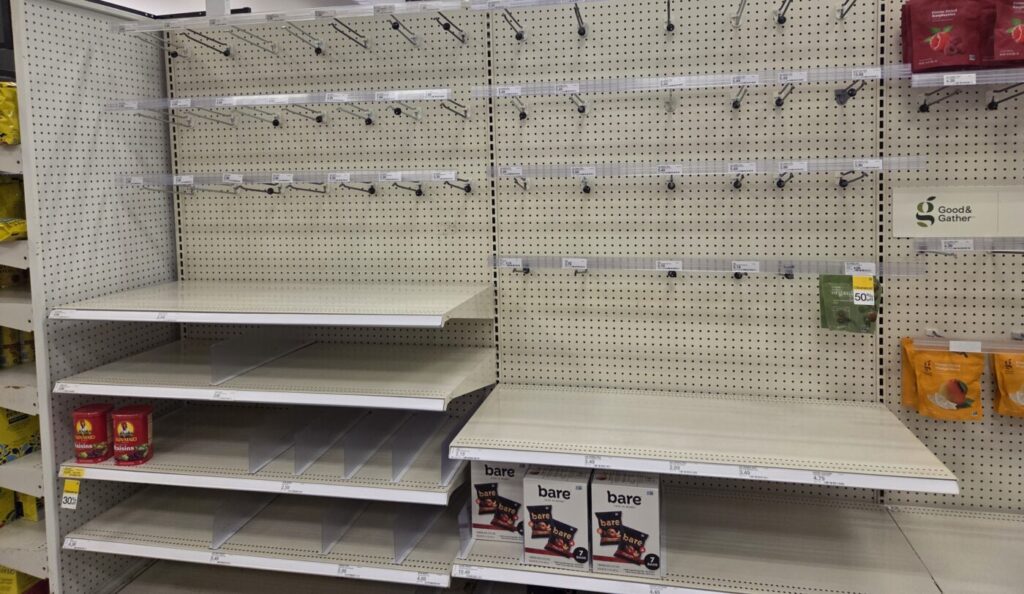 Mostly empty grocery shelf with a few boxes and snack packages left on the ends and lower rows.