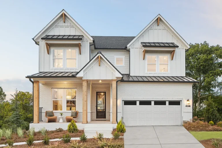 A white two-story house with a front porch, dark roof and two-car garage at dusk.