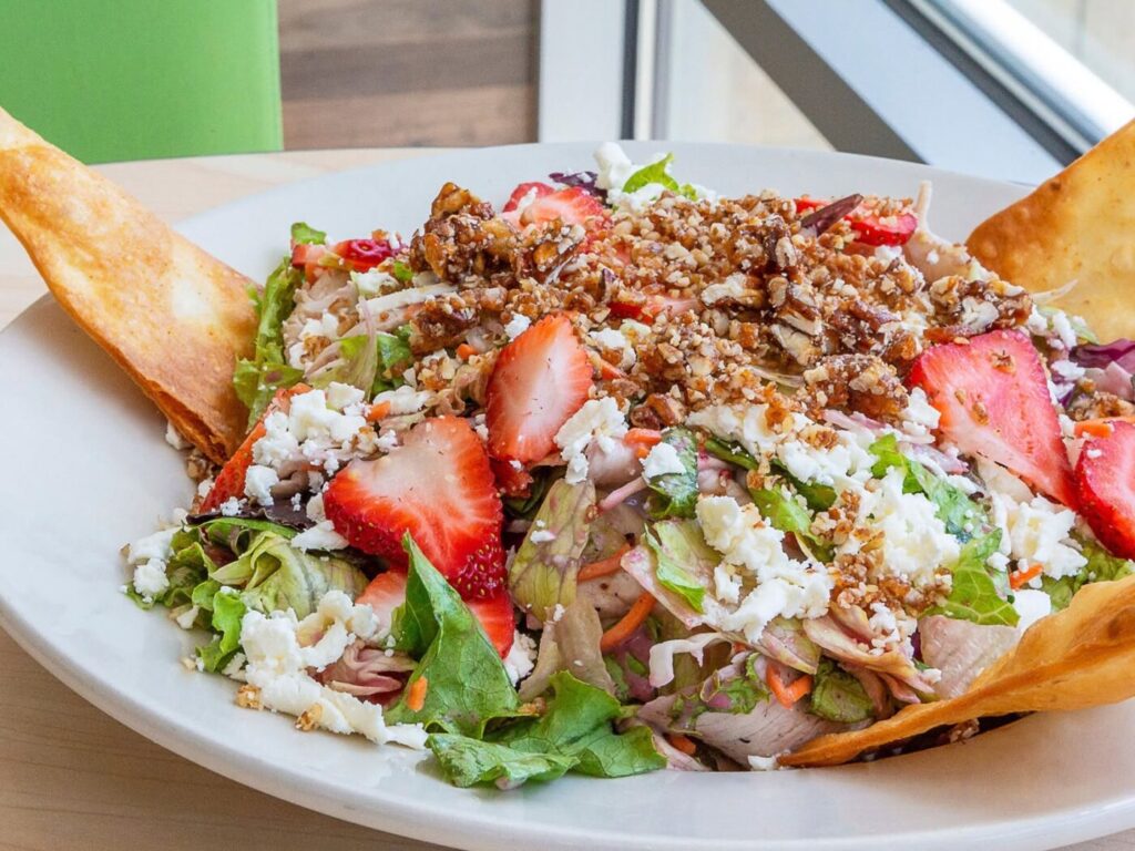 Salad topped with sliced strawberries, crumbled cheese and toasted bread on the side