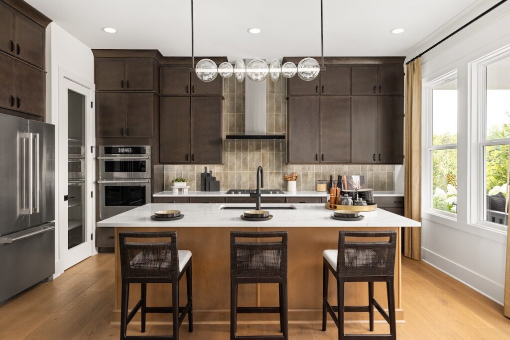 Modern kitchen with dark wood cabinets, a large island, three stools and pendant lights.