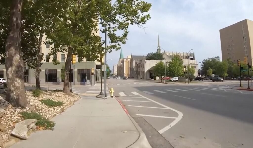 A quiet Tulsa street lined with trees, sidewalks and low-rise buildings.