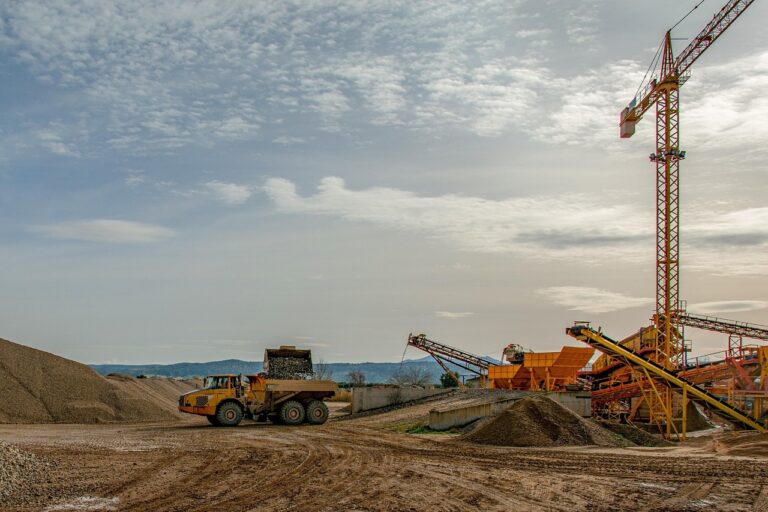 A haul truck loaded with gravel near conveyors and a tall crane at a quarry