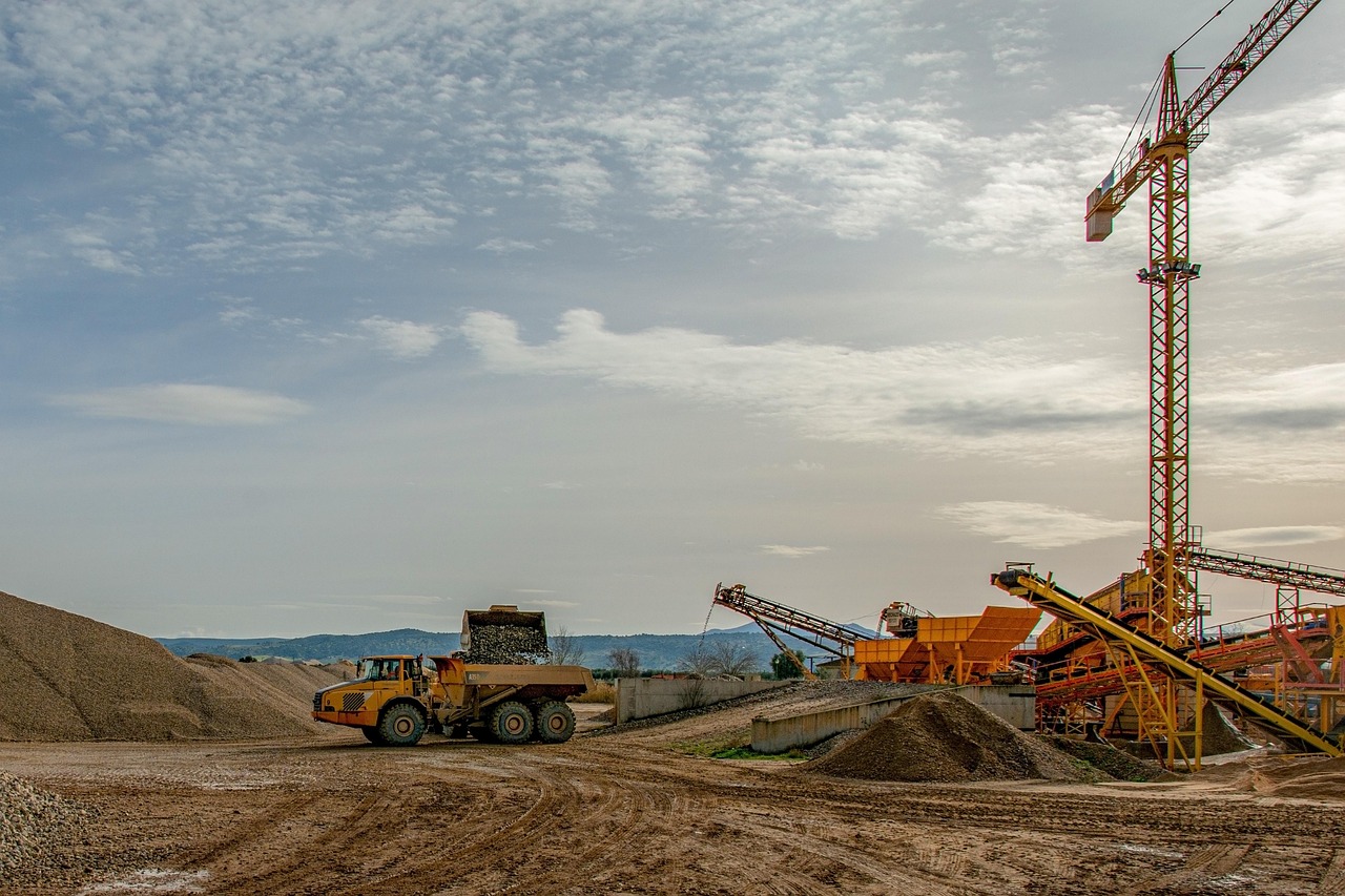 A haul truck loaded with gravel near conveyors and a tall crane at a quarry