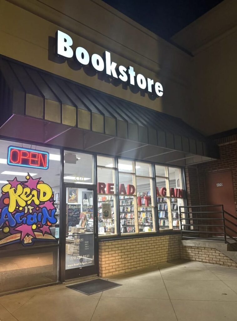 Storefront of Read It Again bookstore at night with an open sign glowing in the window.