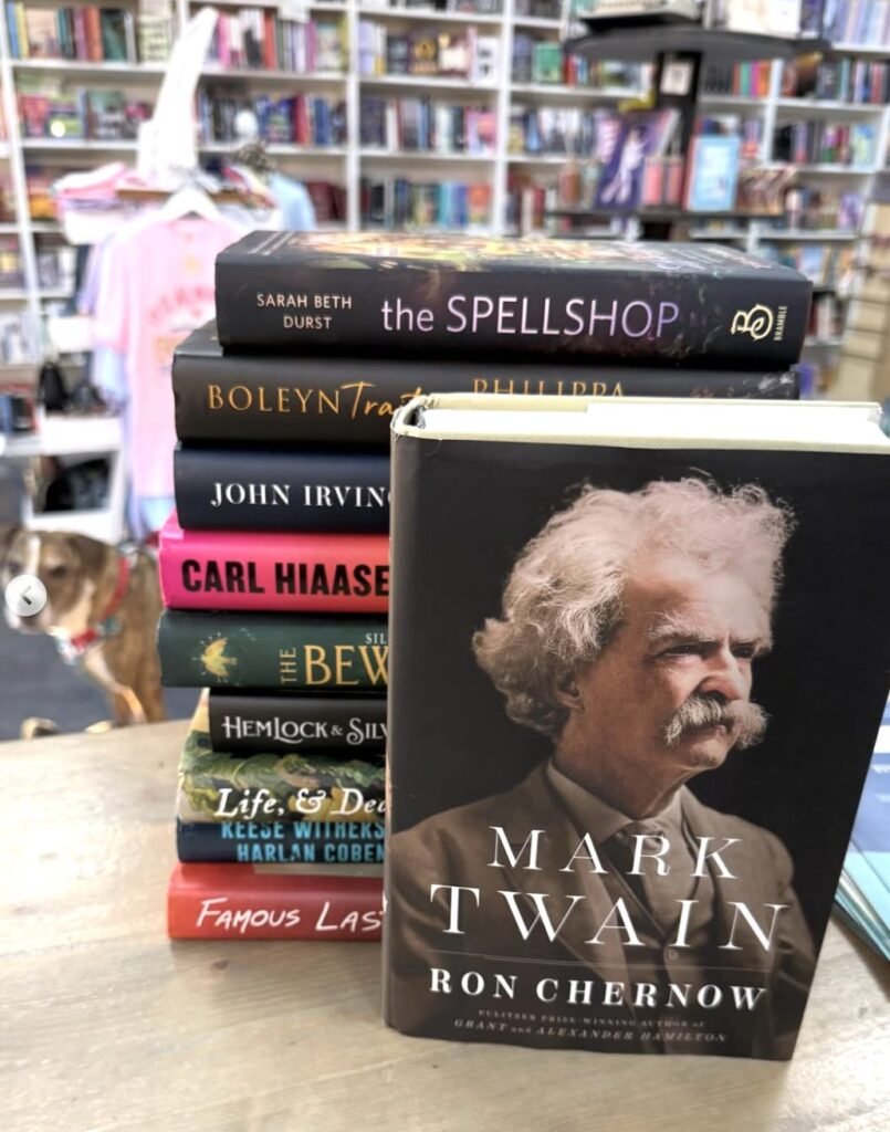 A stack of books with a Mark Twain biography in front, set on a bookstore table.