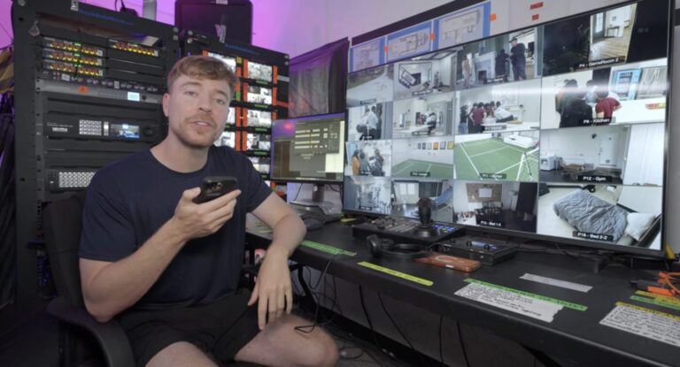 Jimmy Donaldson sits in front of a wall of security monitors and equipment while holding a phone.