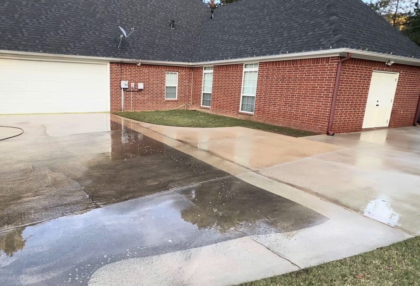 Wet driveway beside a red brick house and garage after cleaning.