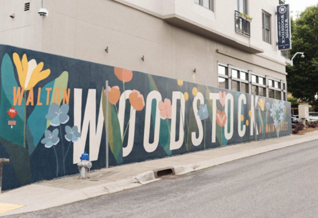 A colorful mural spelling Woodstock runs along the side of a building beside a street.