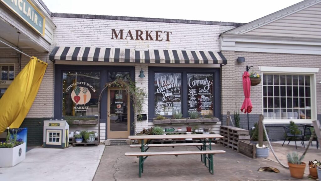 Small market storefront with striped awning, outdoor picnic tables and potted plants