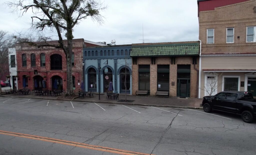Small downtown storefronts across a street, with brick facades and outdoor seating