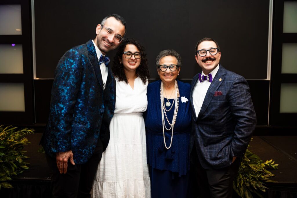 Four people stand together indoors and smile at the camera.