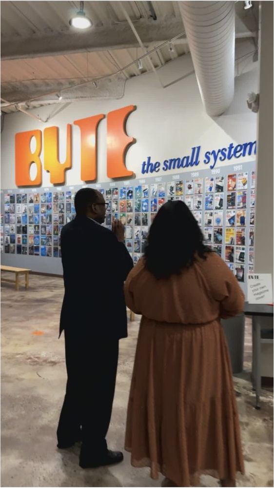 Two visitors stand in front of a wall display with large orange letters reading B Y T the small system.