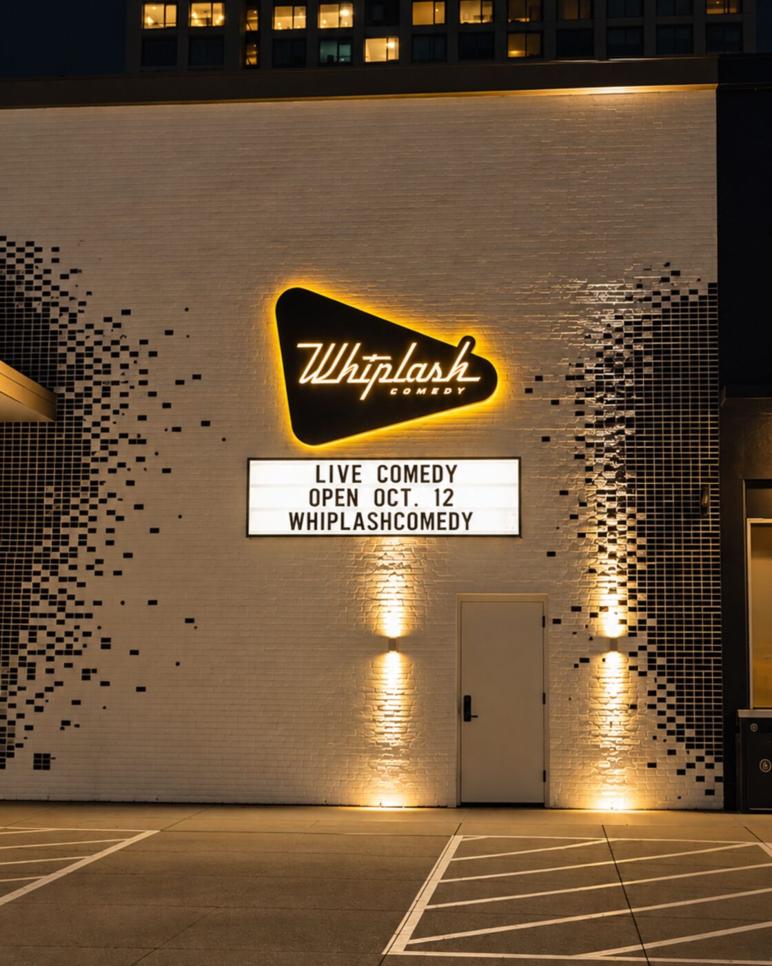 Lit Whiplash Comedy sign on a brick exterior wall with a marquee reading “Live comedy open Oct. 12.”