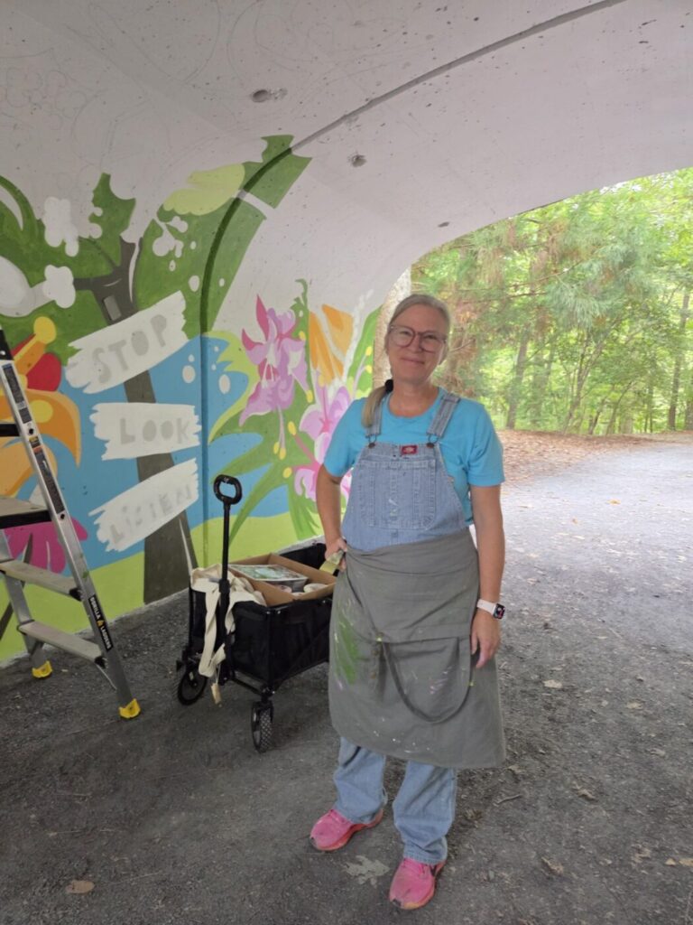 Sarah Emerson stands inside the tunnel beside a painted mural in progress.