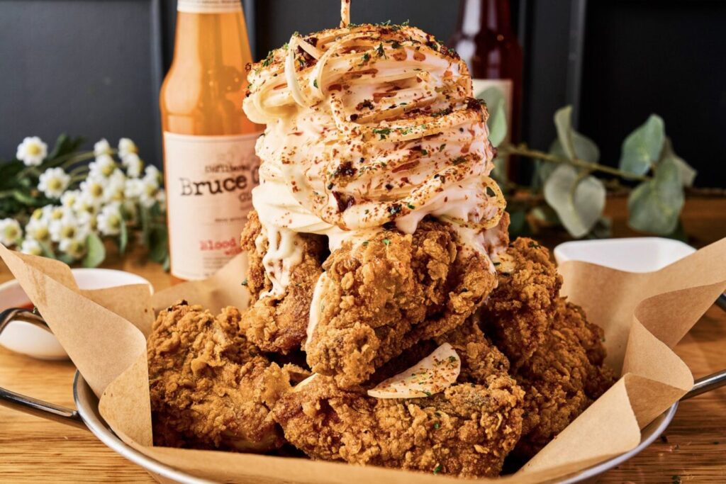 A pile of fried chicken pieces drizzled with pale sauce and scattered with chopped peppers.