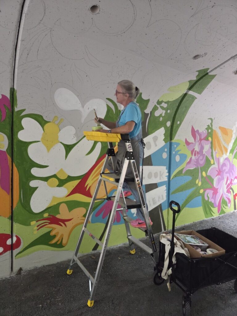 Sarah Emerson paints floral shapes on the tunnel wall from a ladder.