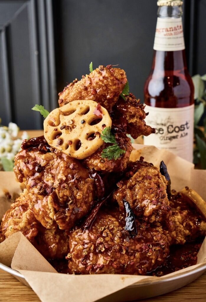A bowl of glazed fried chicken pieces topped with a lotus root chip.