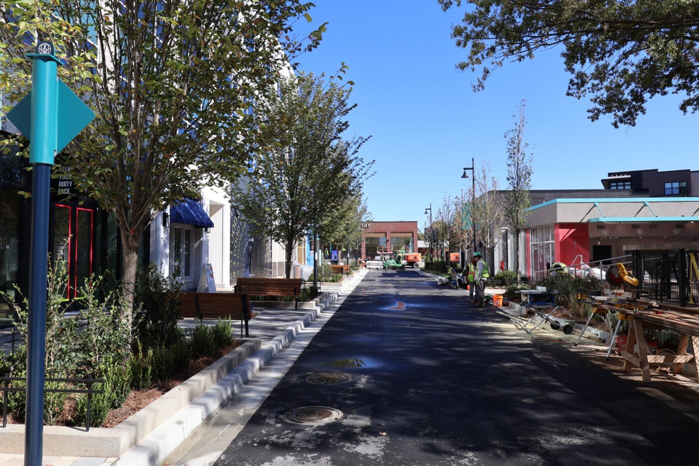 A long view down a landscaped Medley street with benches, storefronts and working crews.