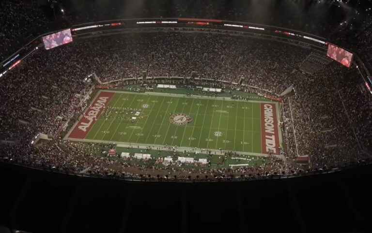 A packed football stadium at night with the field lit and Alabama and Crimson Tide painted in the end zones.