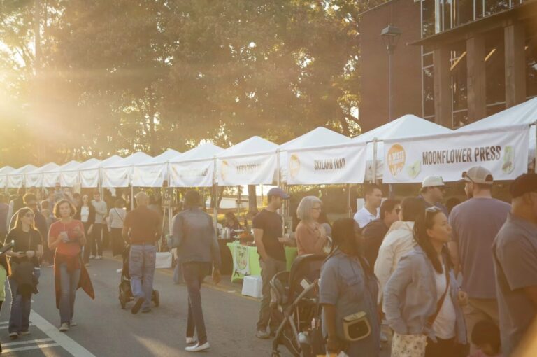 People browse rows of white vendor tents along a street in warm evening light.