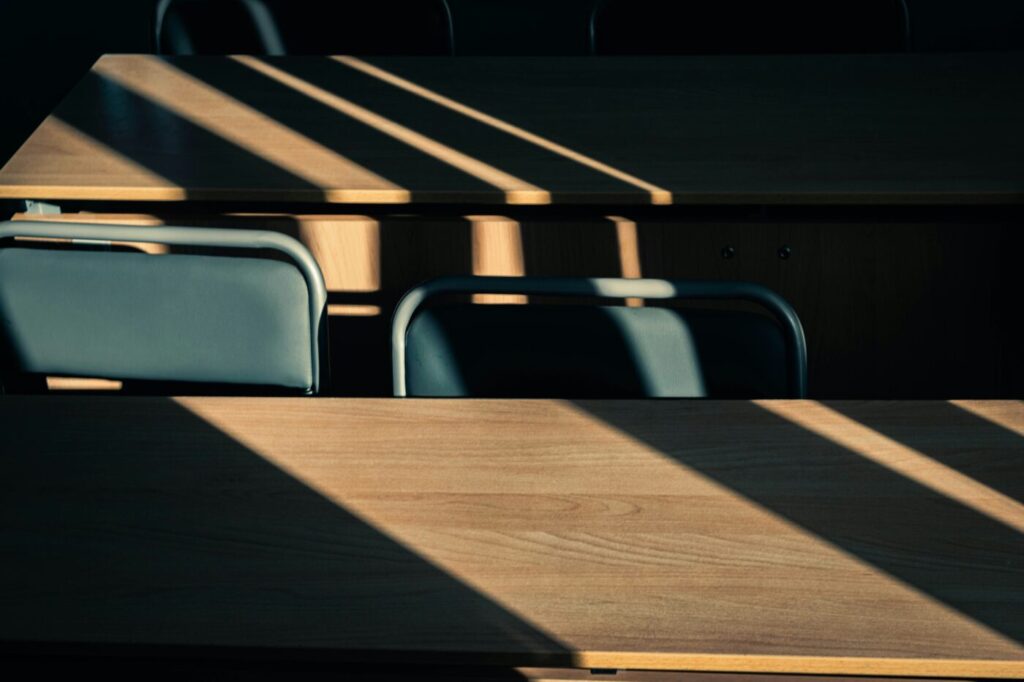 Sunlight falls across the desks of an empty classroom; illustrative education photo by Andrew Bright via Unsplash.