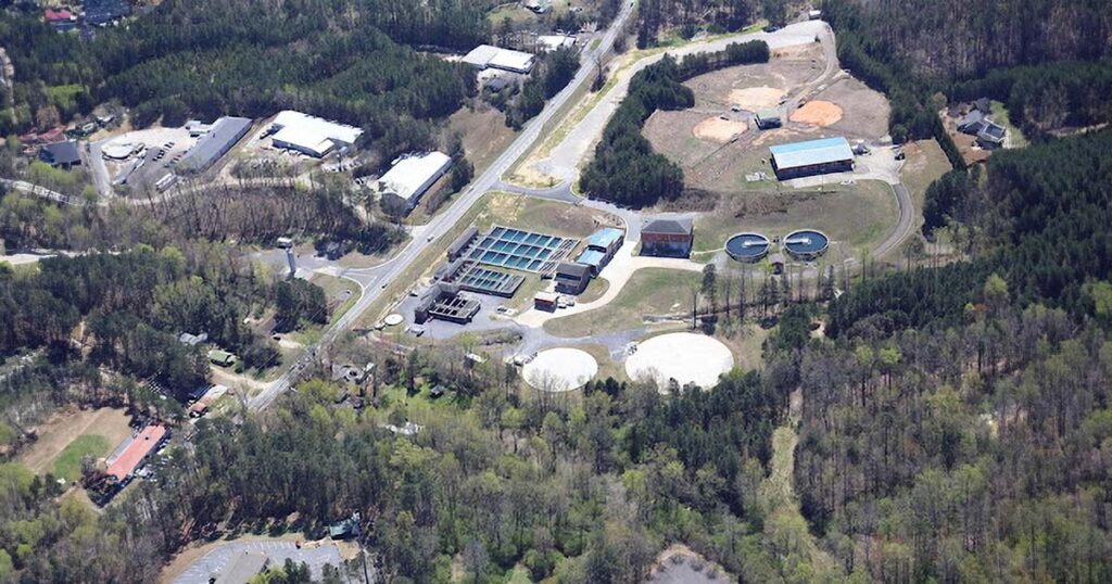 Aerial view of a water-treatment facility with tanks, basins, buildings and surrounding wooded land