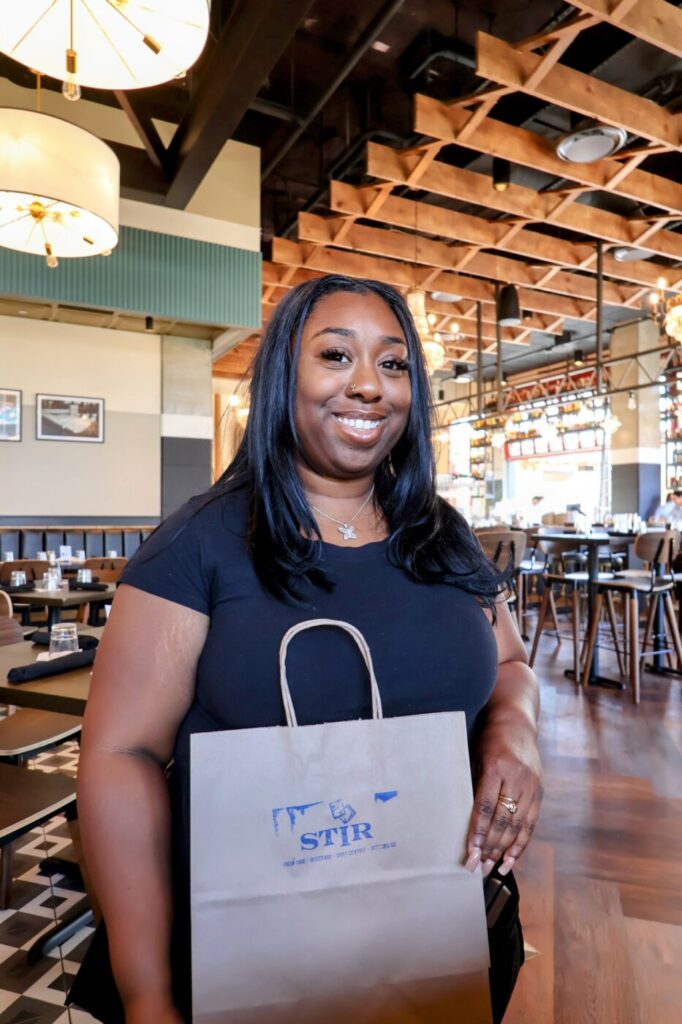 Woman standing inside the restaurant holding a STIR shopping bag