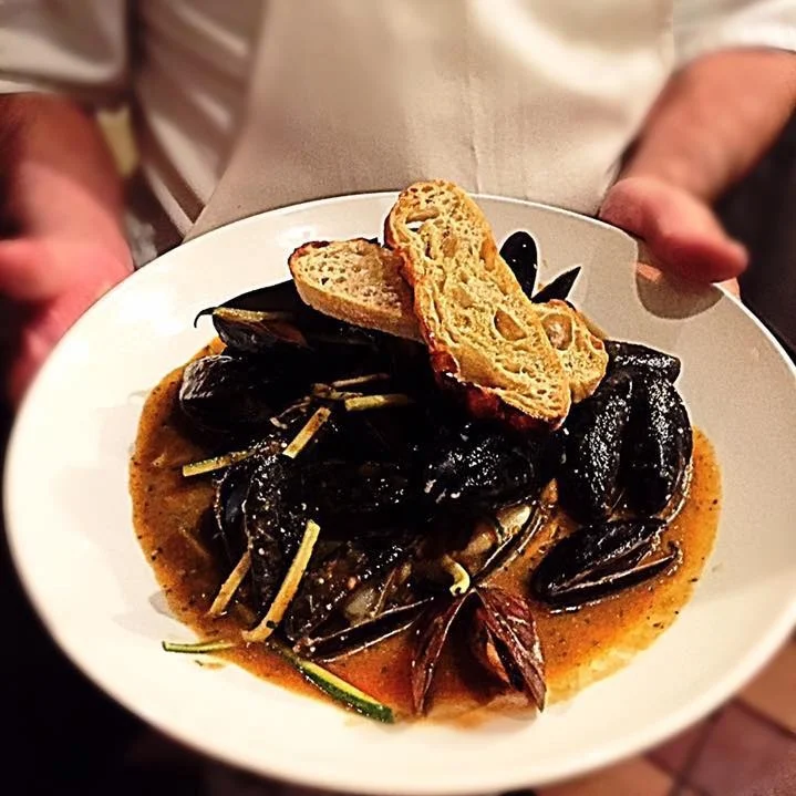 Una persona sostiene un plato de mejillones con pan tostado encima