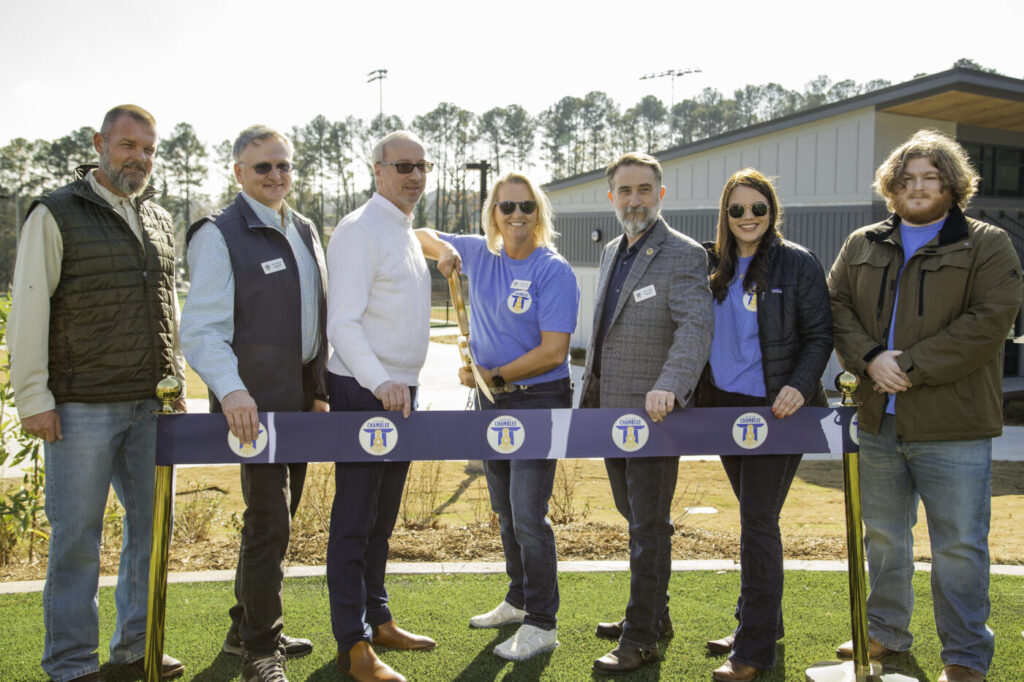 A group of adults stands behind a ribbon at a park opening ceremony.